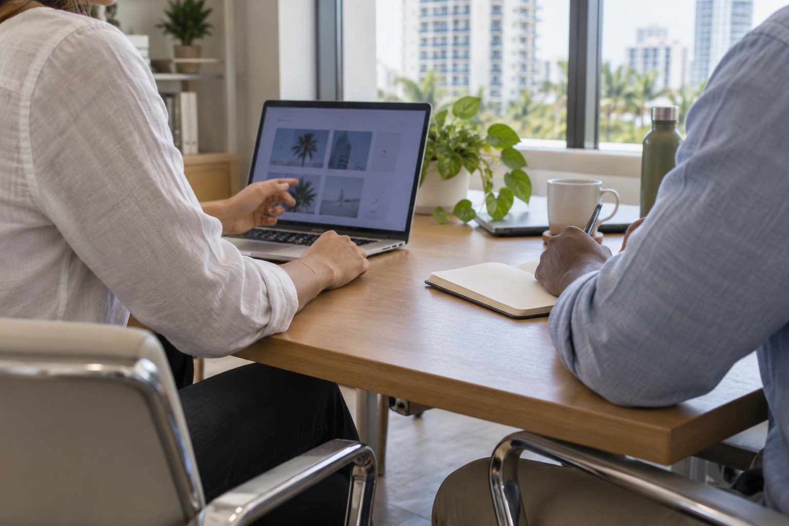 Two coworkers viewed from behind reviewing a laptop and notebook at an office table